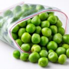Frozen peas spilling from open plastic bag on white background